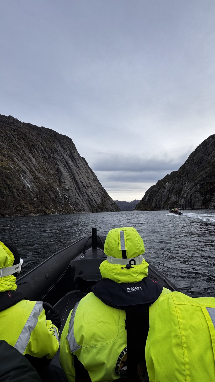 Deltakere i gule flytedresser på ribbåt i en smal fjord med bratte fjellvegger