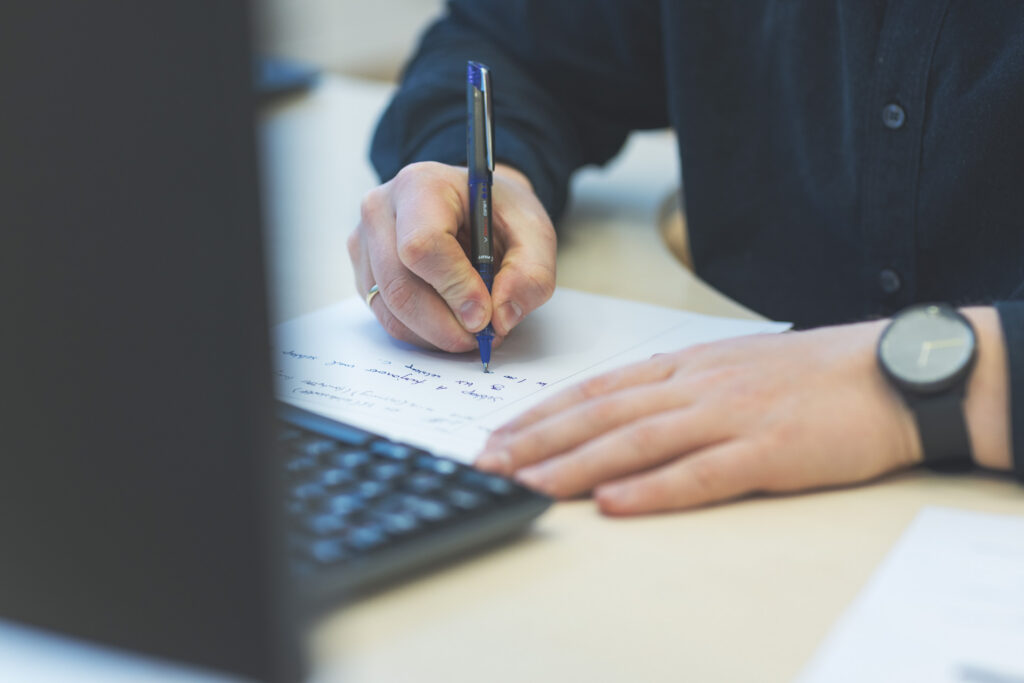 Hender som skriver notater ved siden av tastaturet